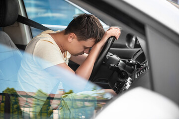 Tired man sleeping on steering wheel in his car