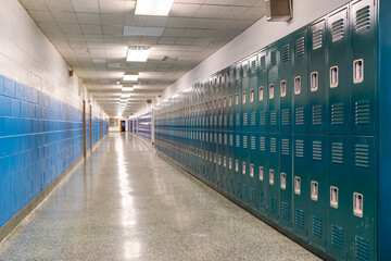 Typical, nondescript USA empty school hallway with teal green metal lockers along one side of the hallway.

