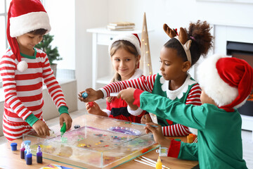 Little children in Christmas costumes pouring paints into water at workshop for Ebru painting