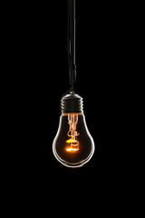 Glowing light bulb hanging on cord against dark background