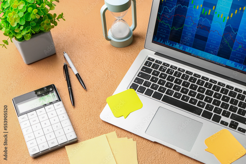 Laptop with sticky notes and calculator on beige background. Trading concept