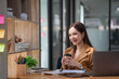 © Songsak C - Beautiful woman holding a coffee cup and using a laptop while sitting at her working place in an office.