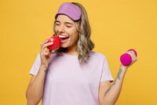 Young Woman She Wear Purple Pyjamas Jam Sleep Eye Mask Rest Relax At Home Hold Dumbbells Biting Apple Fruit Isolated On Plain Yellow Background Studio Portrait Healthy Lifestyle Night Bedtime Concept