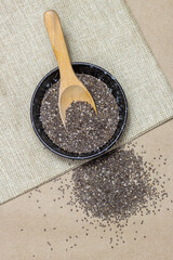 Wall Mural - Healthy food, Chia seeds with spoon in black bowl on linen cloth and heap over cardboard background