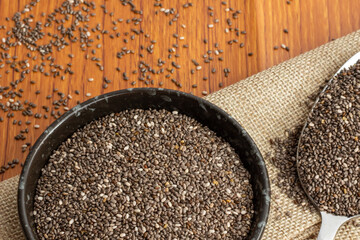 Wall Mural - Healthy breakfast, Chia seeds in black bowl and superfood in spoon falling on wooden background