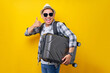 © Bangun Stock Photo - lets go. excited traveler tourist Asian man in casual clothes with hat glasses holding suitcase, showing thumb up on yellow background. Passenger traveling on weekends. Air flight journey concept
