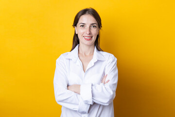 Wall Mural - Smiling young woman in white shirt with arms crossed on yellow background