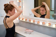 Young ballerina fixing her hair into a bun using bobby pins in front of the mirror.