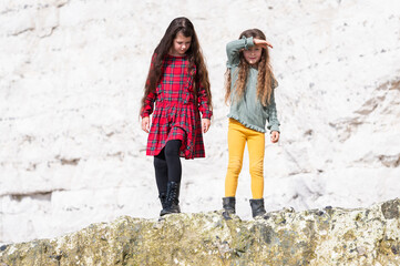 Wall Mural - Two little girls in red tartan dress, green jumper and yellow leggings playing at Hope Gap beach walking on rocks near Cuckmere Haven located between Seaford and Eastbourne in East Sussex, UK