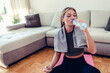 Hydration. Caucasian fit young girl woman in sporty clothes drinking water while sitting in yoga lotus position and watching online tutorial on laptop at home.