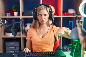 Wall Mural - Young woman playing video games pointing down looking sad and upset, indicating direction with fingers, unhappy and depressed.