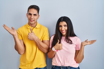 Poster - Young couple standing over isolated background showing palm hand and doing ok gesture with thumbs up, smiling happy and cheerful