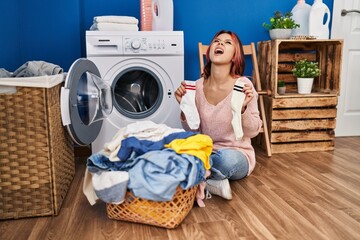 Wall Mural - Young caucasian woman doing laundry holding socks angry and mad screaming frustrated and furious, shouting with anger looking up.