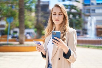 Wall Mural - Young blonde woman using smartphone and credit card at park