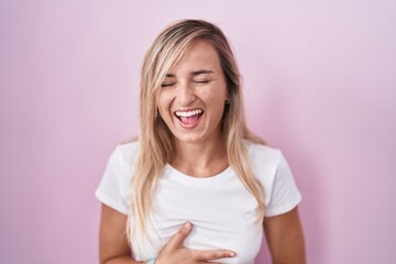 Canvas Print - Young blonde woman standing over pink background smiling and laughing hard out loud because funny crazy joke with hands on body.