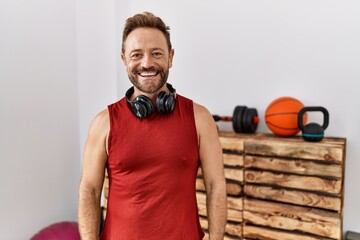 Sticker - Middle age man wearing sportswear and headphones at the gym looking positive and happy standing and smiling with a confident smile showing teeth