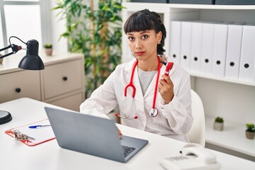 Wall Mural - Young hispanic doctor woman holding ear thermometer thinking attitude and sober expression looking self confident