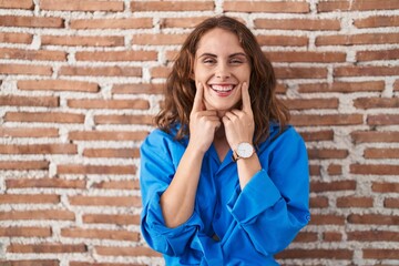 Sticker - Beautiful brunette woman standing over bricks wall smiling with open mouth, fingers pointing and forcing cheerful smile