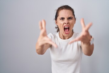 Poster - Beautiful brunette woman standing over isolated background angry and mad raising fists frustrated and furious while shouting with anger. rage and aggressive concept.