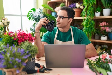 Sticker - Young hispanic man florist holding professional camera using laptop at flower shop