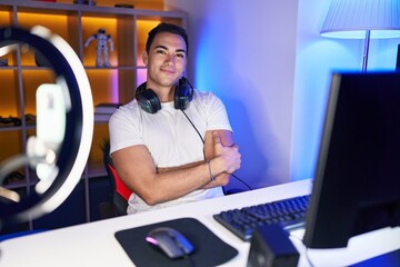 Poster - Young hispanic man streamer smiling confident sitting with arms crossed gesture at gaming room