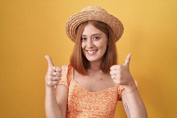 Sticker - Young redhead woman standing over yellow background wearing summer hat success sign doing positive gesture with hand, thumbs up smiling and happy. cheerful expression and winner gesture.