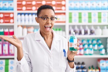 Poster - African american woman working at pharmacy drugstore holding syrup celebrating achievement with happy smile and winner expression with raised hand