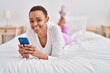 © Krakenimages.com - African american woman using smartphone lying on bed at bedroom