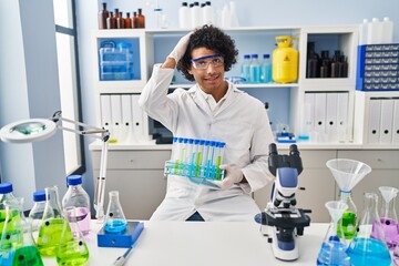 Canvas Print - Hispanic man with curly hair working at scientist laboratory stressed and frustrated with hand on head, surprised and angry face