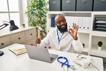 Wall Mural - African american man working at medical clinic holding hammer doing ok sign with fingers, smiling friendly gesturing excellent symbol