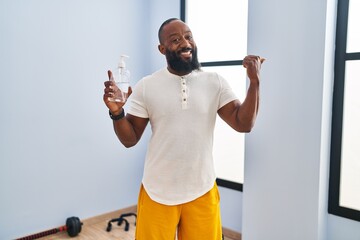 Wall Mural - African american man wearing sportswear holding hydroalcoholic gel pointing thumb up to the side smiling happy with open mouth