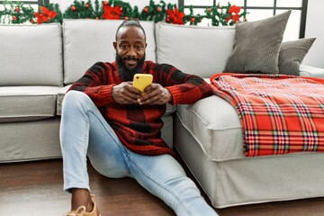 Poster - Young african american man using smartphone sitting by christmas decor at home