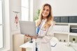 © Krakenimages.com - Young blonde woman wearing doctor uniform using laptop at clinic