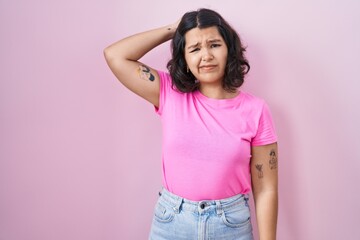 Sticker - Young hispanic woman standing over pink background confuse and wondering about question. uncertain with doubt, thinking with hand on head. pensive concept.