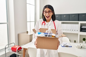Wall Mural - Young hispanic doctor woman holding box with medical items celebrating crazy and amazed for success with open eyes screaming excited.