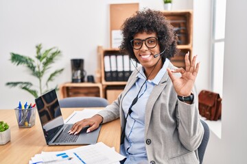 Sticker - Black woman with curly hair wearing call center agent headset at the office smiling positive doing ok sign with hand and fingers. successful expression.