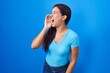 © Krakenimages.com - Young hispanic woman standing over blue background shouting and screaming loud to side with hand on mouth. communication concept.