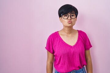 Wall Mural - Young asian woman with short hair standing over pink background looking at the camera blowing a kiss on air being lovely and sexy. love expression.