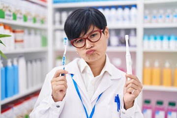 Poster - Young asian woman with short hair doing toothbrush comparative at pharmacy depressed and worry for distress, crying angry and afraid. sad expression.