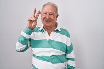 Sticker - Senior man with grey hair standing over white background smiling looking to the camera showing fingers doing victory sign. number two.