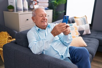 Poster - Middle age grey-haired man using smartphone sitting on sofa at home