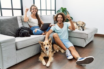 Sticker - Young hispanic couple with dogs relaxing at home smiling amazed and surprised and pointing up with fingers and raised arms.