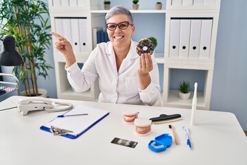 Sticker - Middle age dentist woman holding chocolate doughnut smiling with an idea or question pointing finger up with happy face, number one