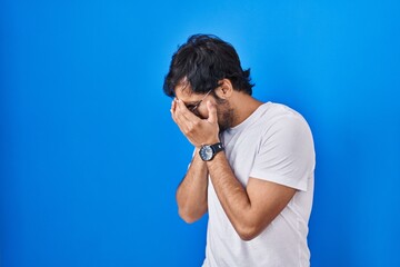 Sticker - Handsome latin man standing over blue background with sad expression covering face with hands while crying. depression concept.