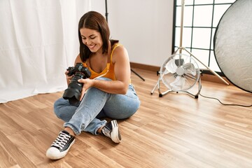 Poster - Young beautiful hispanic woman photographer holding professional camera photo studio