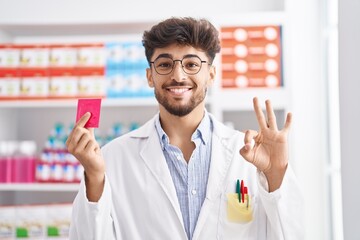 Canvas Print - Arab man with beard working at pharmacy drugstore holding condom smiling looking to the side and staring away thinking.