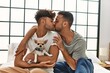 Two hispanic men couple kissing and hugging each other sitting on bed with chihuahua at bedroom