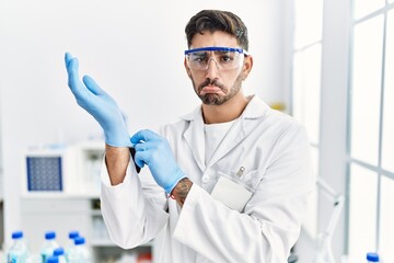 Canvas Print - Young hispanic man working at scientist laboratory putting gloves on depressed and worry for distress, crying angry and afraid. sad expression.