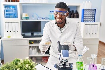 Poster - Young african american man wearing scientist uniform using microscope at laboratory