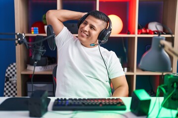 Wall Mural - Young hispanic man playing video games smiling confident touching hair with hand up gesture, posing attractive and fashionable